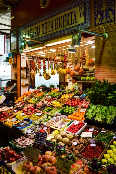 Colorful fruit and vegetable stall in a traditional Spanish market with a vendor behind the counter.