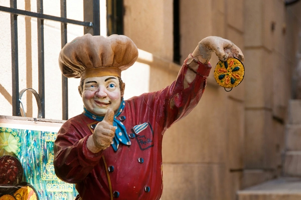 Statue of a cheerful Spanish chef holding a miniature paella and giving a thumbs up outside a local restaurant.