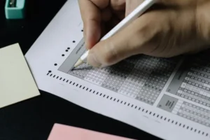 A close-up of a student's hand using a pencil to fill out a multiple-choice answer sheet for a Spanish language exam, representing the DELE certification process.