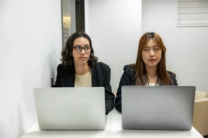 Two expats sitting with laptops in a Madrid office, exchanging uncertain looks that represent the frustration of navigating life in Spain without Spanish.