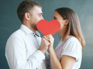 Un hombre y una mujer con camisas blancas sostienen un corazón de papel rojo entre ellos, simbolizando la naturaleza emocional y romántica del idioma español.