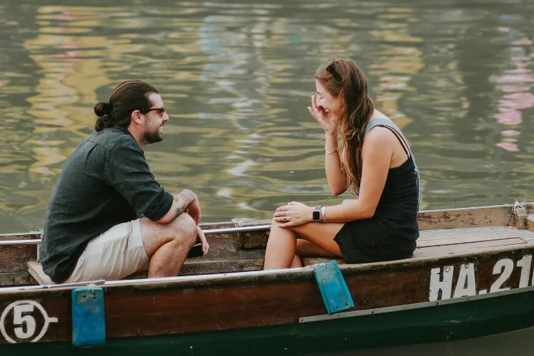 A man and a woman sitting across from each other on a boat, sharing a joyful and expressive conversation.