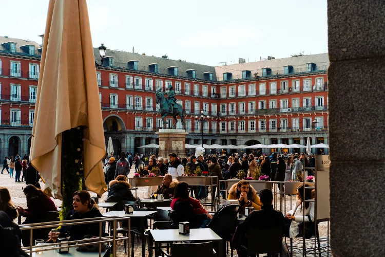 A bustling scene at Plaza Mayor in Madrid with people enjoying outdoor cafés near the statue of King Philip III, representing daily life in the city.
