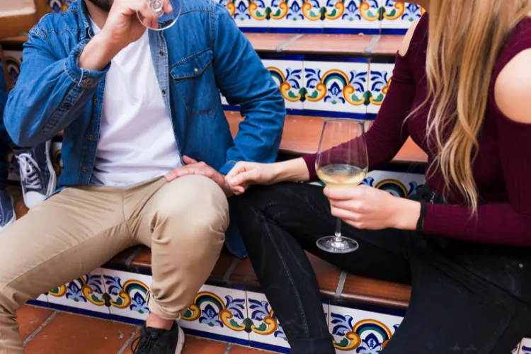 A man in a denim shirt and a woman in a burgundy top sitting on traditional tiled stairs in Madrid, sharing wine and a moment of closeness.