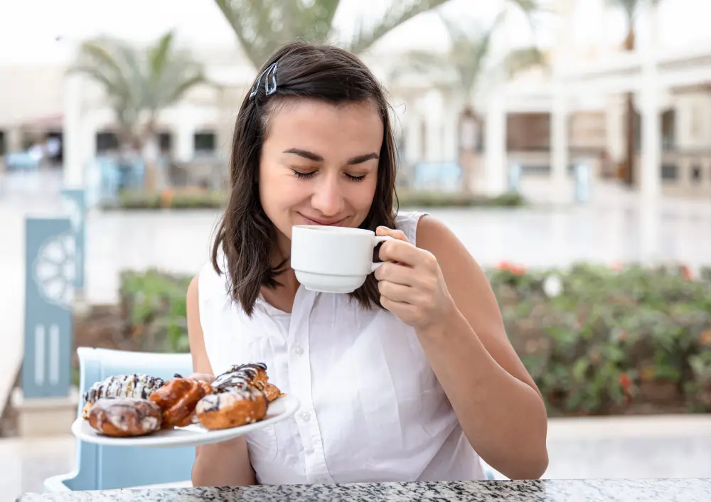 A woman smiling while enjoying a morning coffee and pastries at an outdoor cafe, representing the start of the daily work rhythm in Madrid.