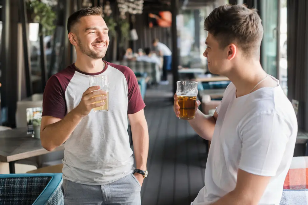 Two men smiling and chatting casually while holding beer glasses inside an open-air terrace bar in Madrid.