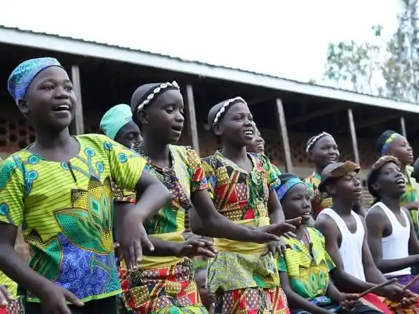 Children singing and dancing in colorful traditional dress at a cultural performance supported by LAE Madrid and Kelele África