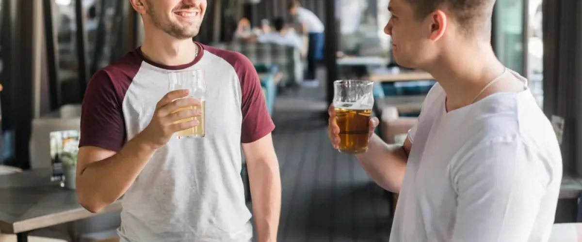 Two men smiling and chatting casually while holding beer glasses inside an open-air terrace bar in Madrid.