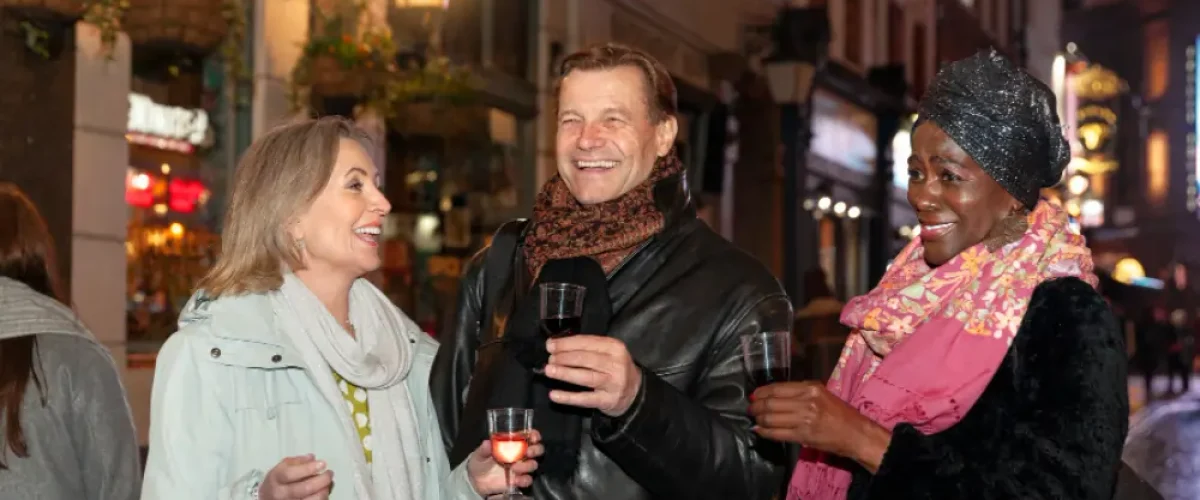A diverse group of friends laughing and enjoying drinks on a brightly lit Madrid street at night, illustrating the late-night social culture and evening energy.