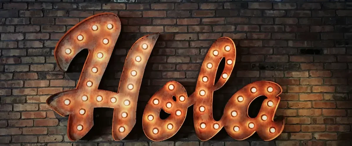 A vintage-style neon "Hola" sign on a brick wall in a Madrid cafe, representing the first step in learning Spanish and building confidence.
