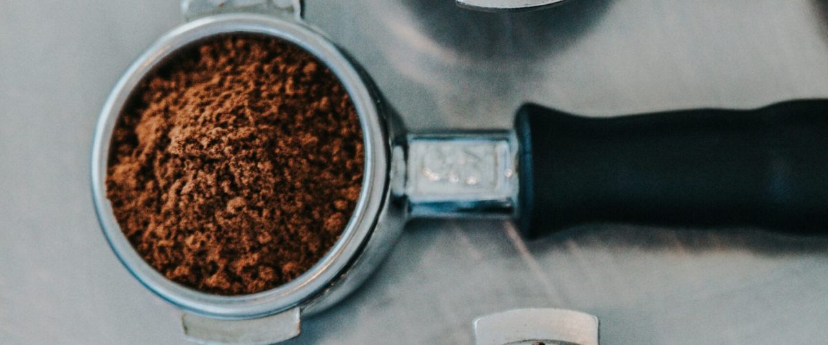 Three metal portafilters showing coffee beans, ground coffee, and a finished cappuccino with latte art — representing Spanish coffee culture and café traditions in Madrid.