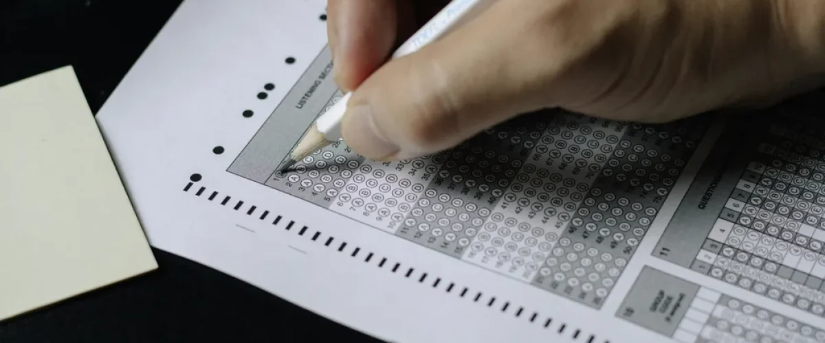 A close-up of a student's hand using a pencil to fill out a multiple-choice answer sheet for a Spanish language exam, representing the DELE certification process.