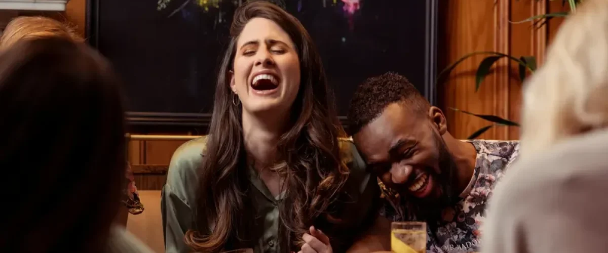 A diverse group of friends laughing and enjoying drinks at a traditional Madrid bar, illustrating social integration through Spanish language skills.