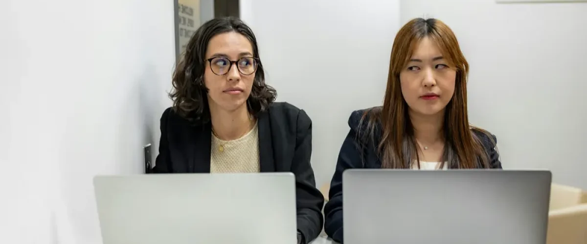 Two expats sitting with laptops in a Madrid office, exchanging uncertain looks that represent the frustration of navigating life in Spain without Spanish.