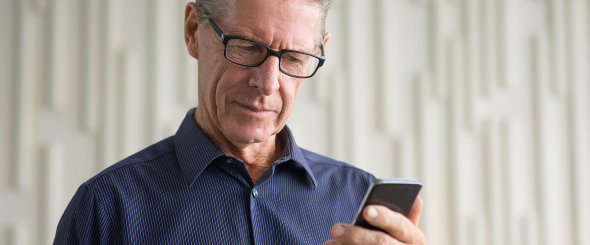 Un hombre con gafas y camisa azul mira intensamente la pantalla de su smartphone, practicando vocabulario de español a través de una aplicación